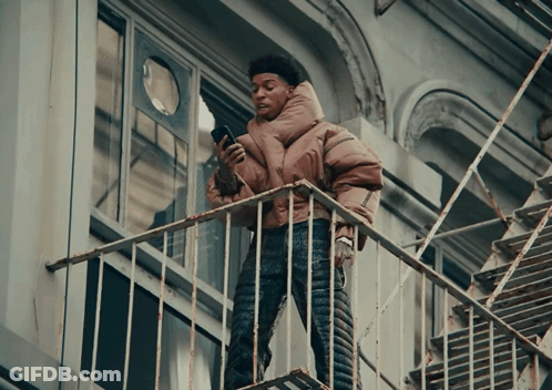 A Person Standing On A Fire Escape Looking At A Cell Phone GIF