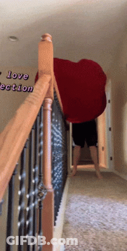 A Person Standing On A Set Of Stairs Holding A Large Red Heart Shaped Blanket GIF