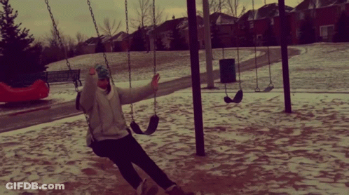 A Person Swinging On A Swing Set In A Snowy Park GIF
