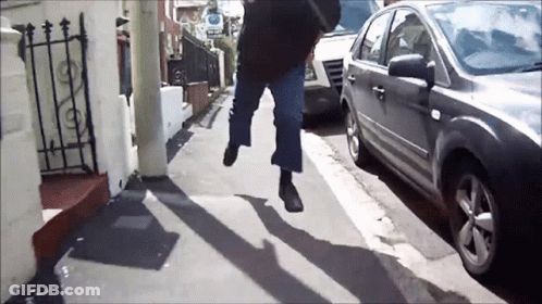 A Person Walking Down A Street With A Car Parked On The Side GIF