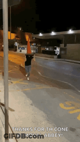 A Person Walking Down A Street With A Traffic Cone On Their Head And The Words Thanks For The Cone Removal Abbey GIF