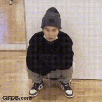 A Person Wearing A Beanie And A Sweater Is Squatting Down On The Floor . GIF