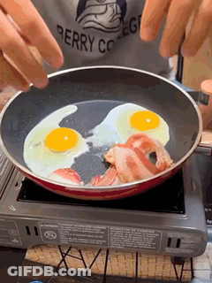 A Person Wearing A Berry College Shirt Is Cooking Eggs And Bacon GIF