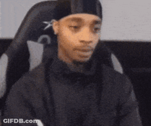 A Person Wearing A Black Hat Is Sitting In A Chair GIF