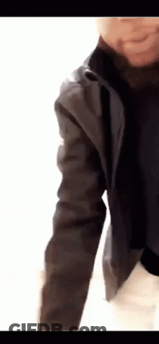 A Person Wearing A Black Jacket And A Black Turtleneck Is Standing On A White Surface . GIF