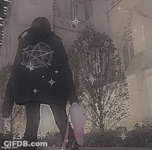 A Person Wearing A Black Jacket With A Pentagram On The Back Is Standing In Front Of A Building . GIF