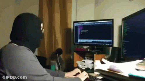A Person Wearing A Black Mask Is Typing On A Keyboard In Front Of Two Computer Monitors GIF