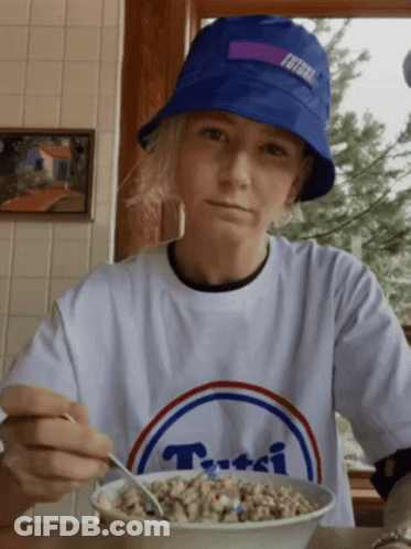 A Person Wearing A Blue Hat And A White T-Shirt With The Word Tutti On It Is Eating Cereal GIF