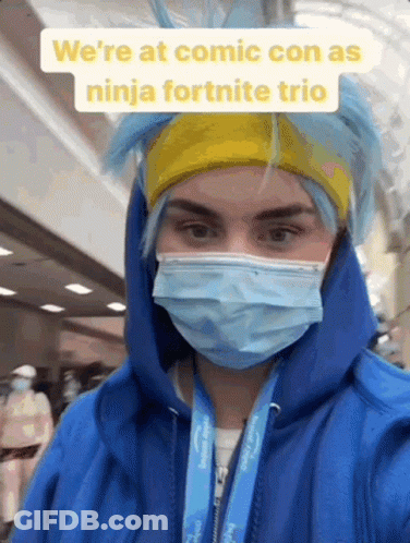 A Person Wearing A Blue Hoodie And A Mask Is Standing In A Hallway . GIF