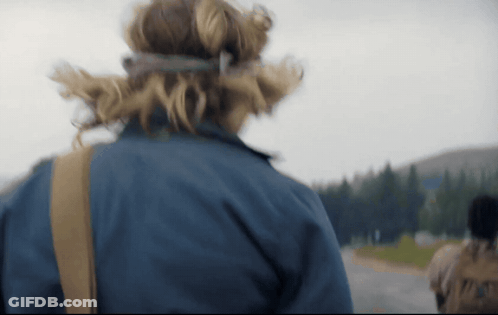 A Person Wearing A Blue Jacket Is Walking Down A Road With Trees In The Background GIF