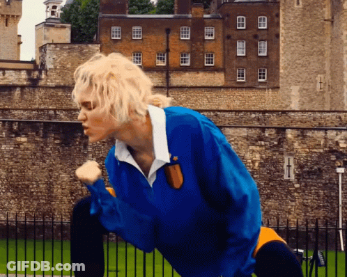 A Person Wearing A Blue Jacket Stands In Front Of A Brick Building GIF