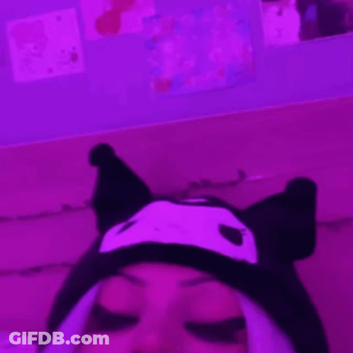 A Person Wearing A Cat Hat Is Laying On A Couch In A Pink Room . GIF