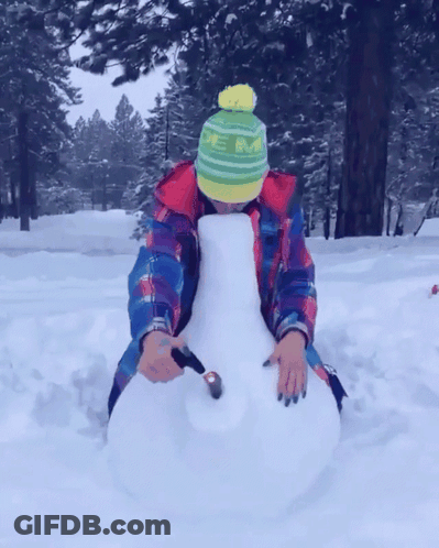 A Person Wearing A Green And Yellow Hat With The Letter M On It Is Sitting In The Snow GIF