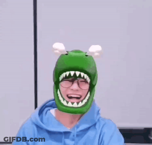 A Person Wearing A Green Dinosaur Hat With A Mouth And Teeth On It . GIF
