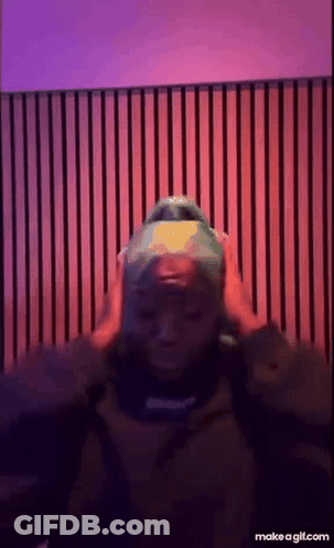 A Person Wearing A Green Hat Is Standing In Front Of A Purple And Red Wall . GIF