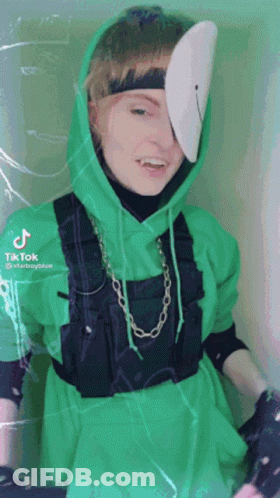A Person Wearing A Green Hoodie And Overalls With A Mask On Their Face . GIF