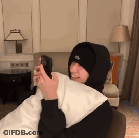 A Person Wearing A Hooded Sweatshirt And A Hat With The Letter S On It Is Holding A Cell Phone GIF