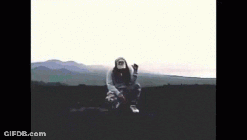 A Person Wearing A Hoodie And A Hat Is Sitting In The Middle Of A Field GIF