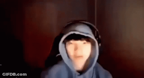 A Person Wearing A Hoodie And Headphones Is Sitting In A Dark Room . GIF