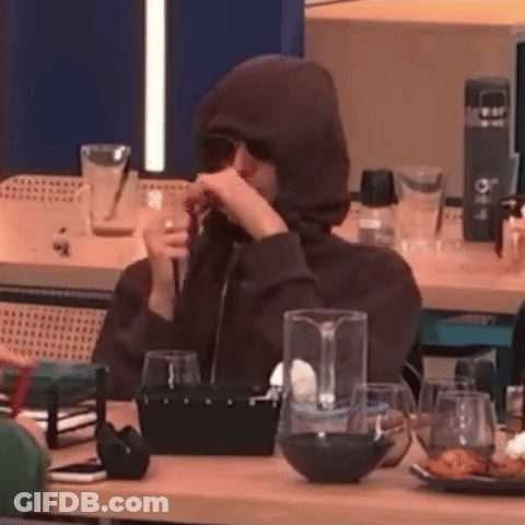 A Person Wearing A Hoodie And Sunglasses Is Sitting At A Table Drinking A Glass Of Wine . GIF
