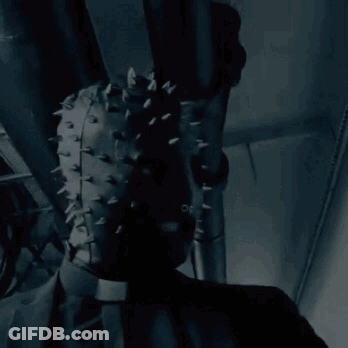 A Person Wearing A Leather Mask With Spikes On It Is Hanging From A Pipe . GIF