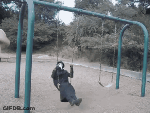A Person Wearing A Mask Sits On A Swing In A Park GIF