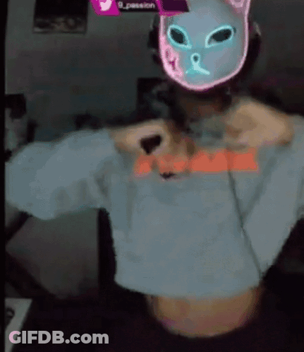 A Person Wearing A Neon Cat Mask And A Crop Top Is Taking Off Their Shirt . GIF