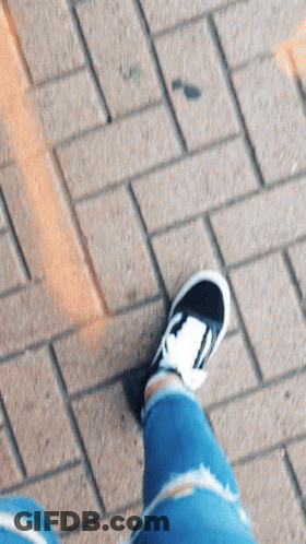 A Person Wearing A Pair Of Black And White Sneakers Is Standing On A Brick Sidewalk GIF