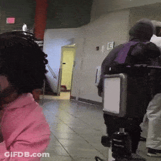 A Person Wearing A Pink Hoodie Is Standing In A Hallway With A Camera GIF