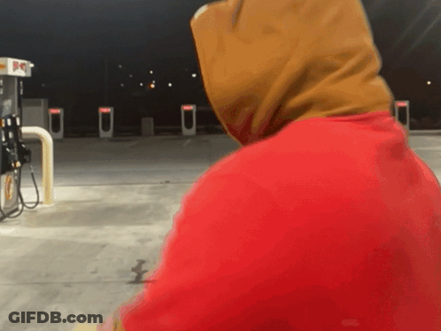 A Person Wearing A Red Hoodie Stands In Front Of A Gas Pump GIF