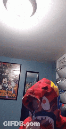 A Person Wearing A Red Shark Hoodie In A Room With A Poster That Says My Hero Academia GIF
