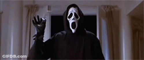A Person Wearing A Scream Mask And A Hooded Jacket Is Standing In A Dark Room . GIF