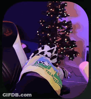 A Person Wearing A Shirt That Says Music Television Is Laying In Front Of A Christmas Tree GIF