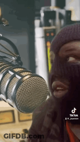 A Person Wearing A Ski Mask Stands In Front Of A Microphone . GIF
