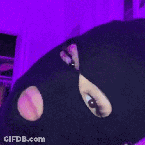 A Person Wearing A Ski Mask With Holes In It Is Standing In Front Of A Purple Wall GIF