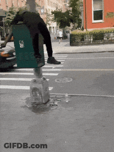 A Person Wearing A Trash Can On Their Back Is Crossing The Street GIF