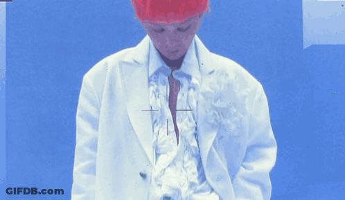 A Person Wearing A White Jacket And A Red Hat Stands In Front Of A Blue Background GIF