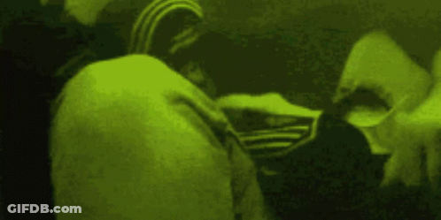 A Person Wearing An Adidas Jacket Is Standing In A Dark Room With A Green Background . GIF