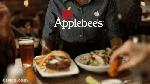 A Person Wearing An Applebee 'S Shirt Is Sitting At A Table With Food GIF