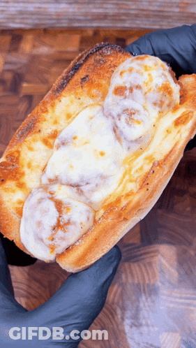 A Person Wearing Black Gloves Is Holding A Meatball Sub With Cheese GIF