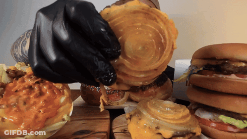 A Person Wearing Black Gloves Is Holding A Piece Of Cheese On A Hamburger GIF