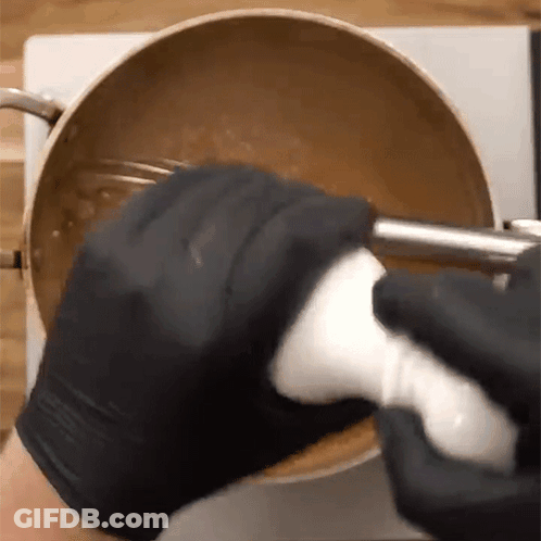 A Person Wearing Black Gloves Is Mixing Something In A Pot With A Blender . GIF