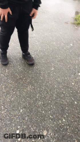 A Person Wearing Black Pants And Black Shoes Is Standing On A Concrete Surface GIF