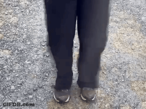 A Person Wearing Black Pants And Brown Shoes Is Standing On A Gravel Path GIF