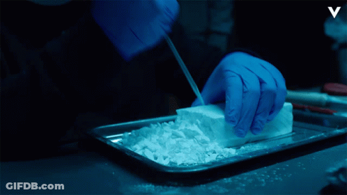 A Person Wearing Blue Gloves Is Cutting Up A Piece Of White Powder GIF