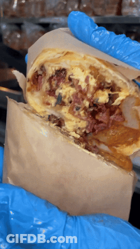 A Person Wearing Blue Gloves Is Holding A Burrito With Meat And Eggs GIF