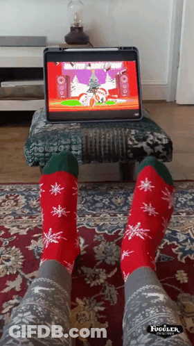 A Person Wearing Christmas Socks Is Sitting In Front Of A Computer GIF