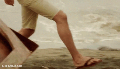 A Person Wearing Flip Flops Is Walking On A Sandy Beach GIF