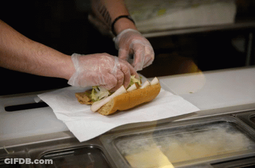 A Person Wearing Plastic Gloves Prepares A Sandwich GIF