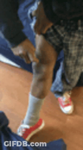 A Person Wearing Red Shoes And White Socks Is Standing On A Wooden Floor And Pointing At Their Knee . GIF